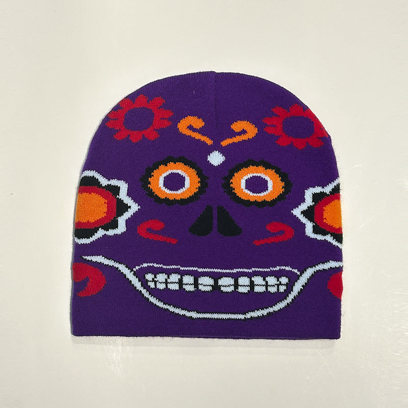 Purple beanie with a colorful Day of the Dead skull design, featuring orange, red, and black floral and facial patterns, including eyes and teeth on a light background.