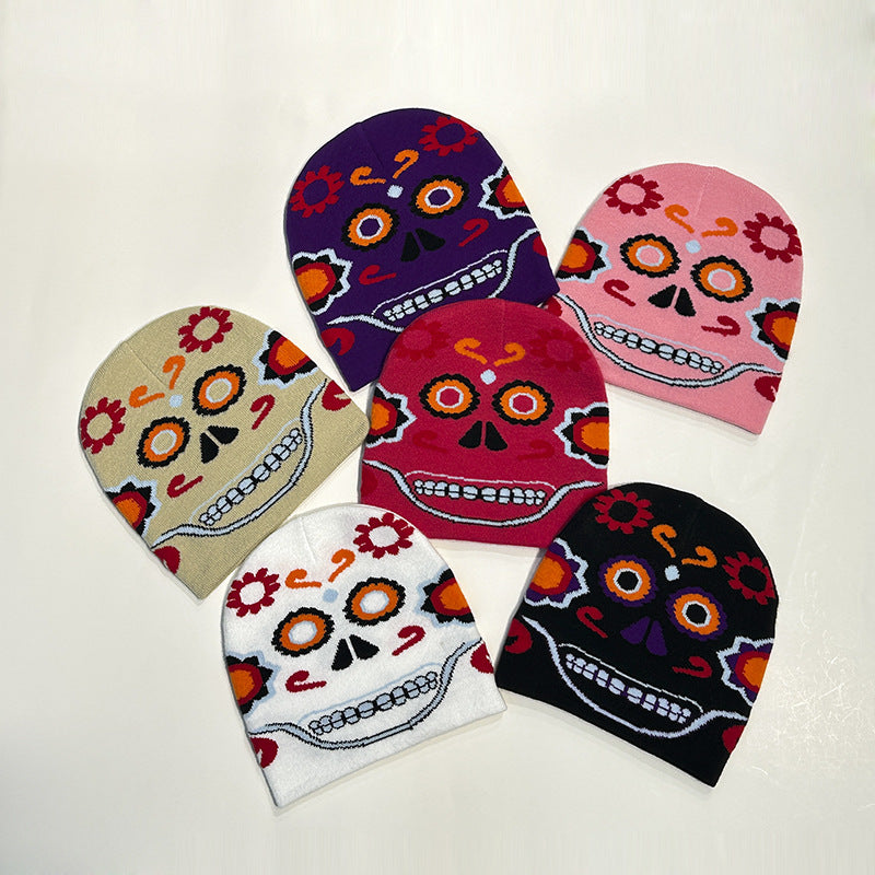 Five colorful beanies featuring a Day of the Dead skull design with flowers. The beanies are in beige, white, black, pink, and purple, arranged on a plain background.