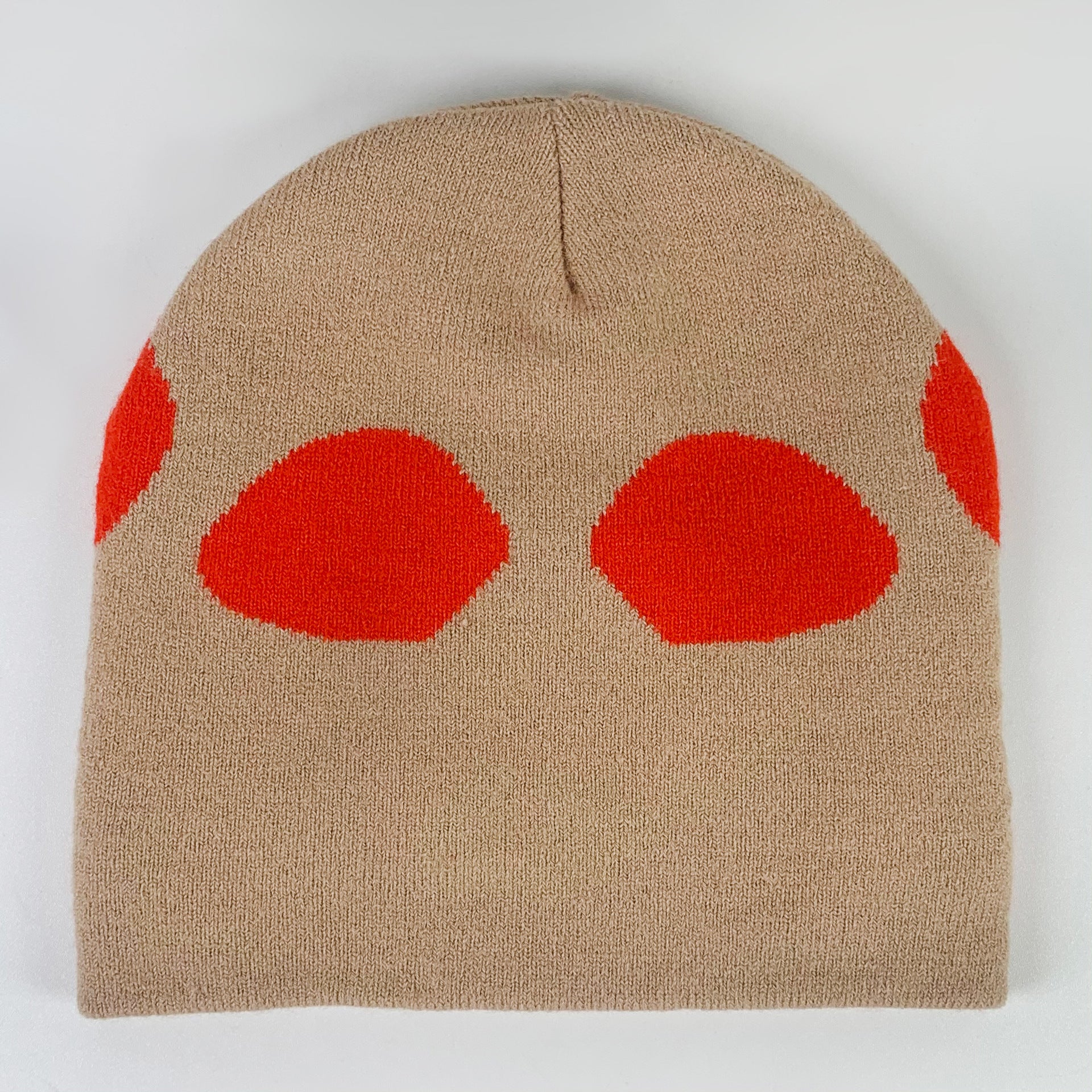 A beige knit beanie featuring bold red abstract shapes arranged in a symmetrical pattern, creating a modern and striking design.