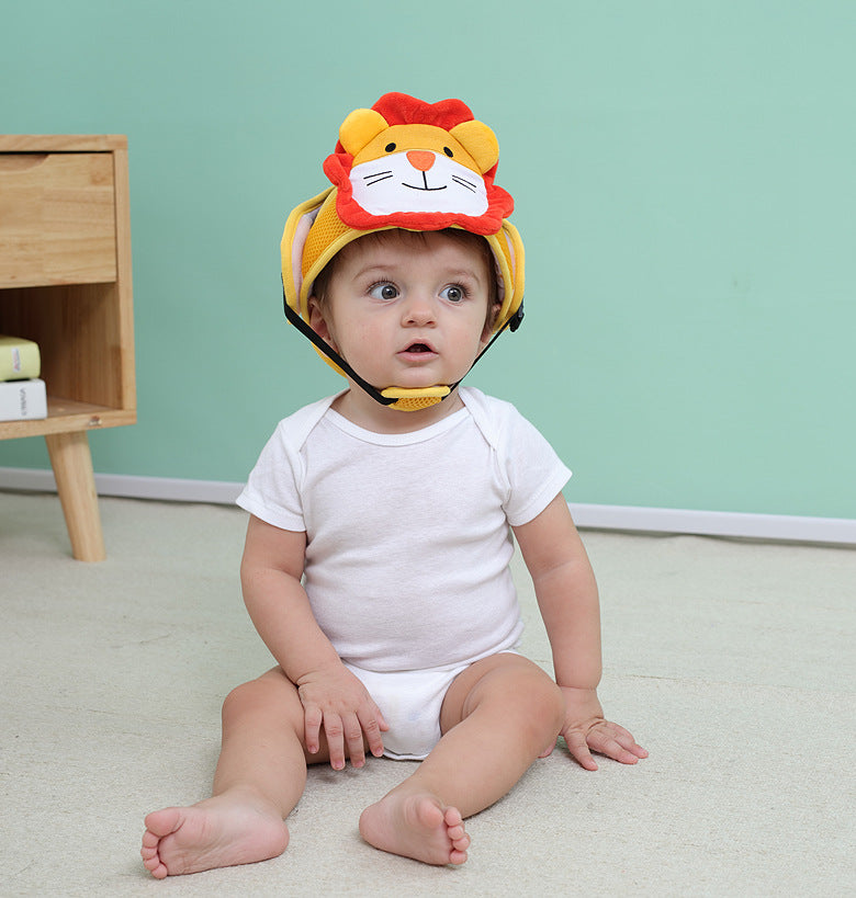 Baby sitting on the floor wearing a white onesie and a lion-themed padded helmet, in front of a light green wall with a wooden side table nearby.