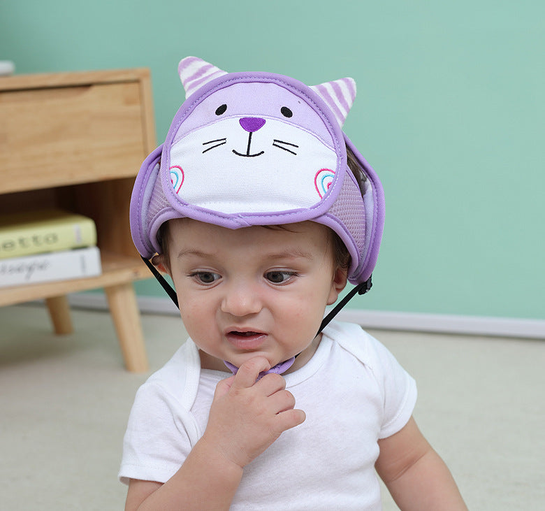 A baby wearing a soft, purple helmet with a cute cat face design. The helmet has ears and a chinstrap. The baby is dressed in a white shirt, sitting in a room with pastel walls.