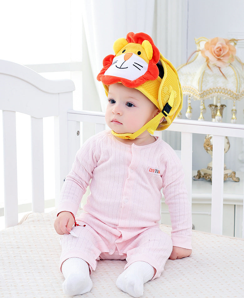 A baby in a pink onesie sits in a crib, wearing a yellow helmet with a lion design. A vintage lamp with a pink flower decoration is in the background.