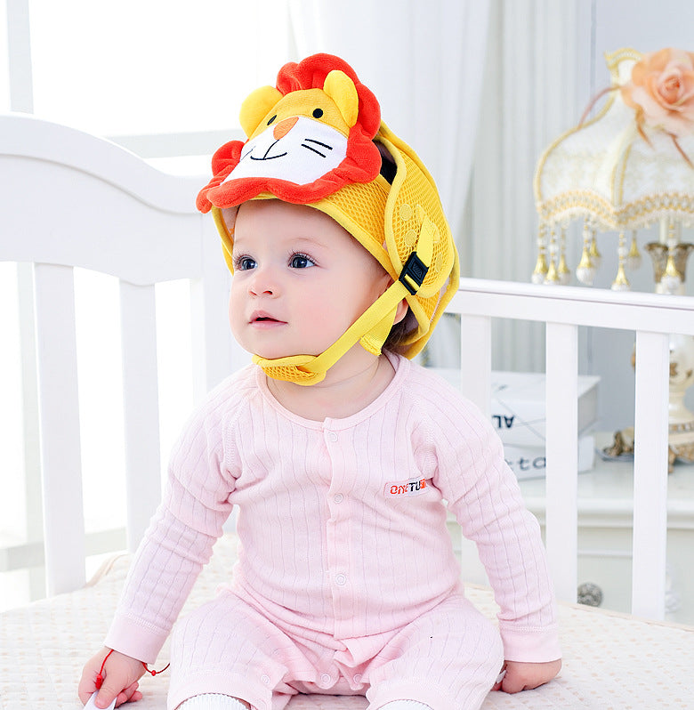 A baby in a pink onesie sits in a crib, wearing a yellow helmet with a cute lion face design. A decorative lamp and a flower are in the background.
