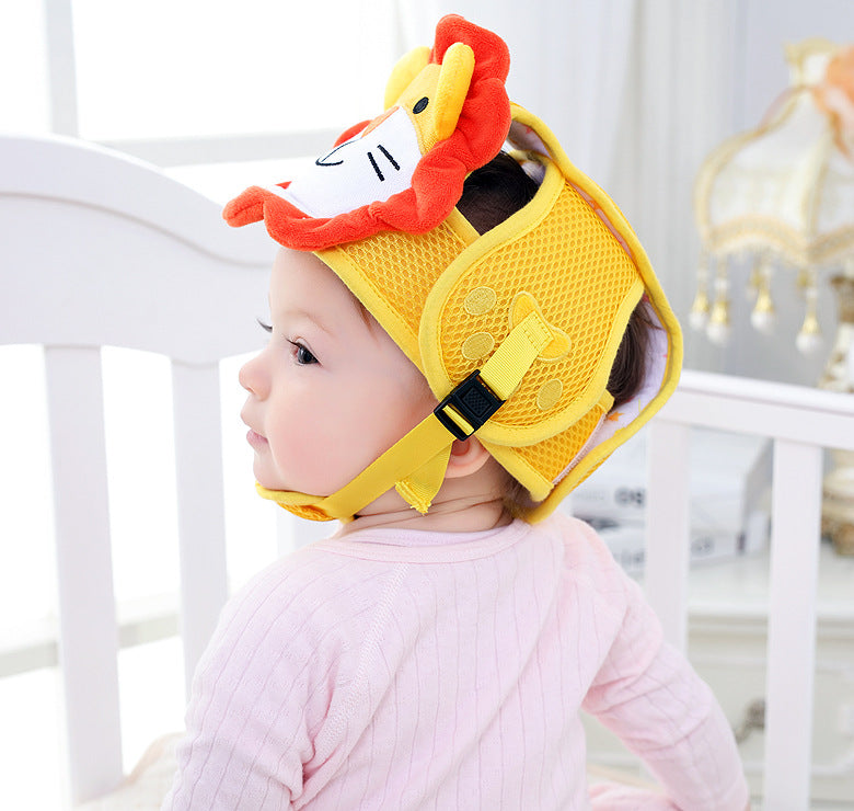 A baby in a pink shirt sits in a crib wearing a colorful protective helmet with a cartoon lion design, featuring a yellow mesh and red mane. A soft light fills the room.