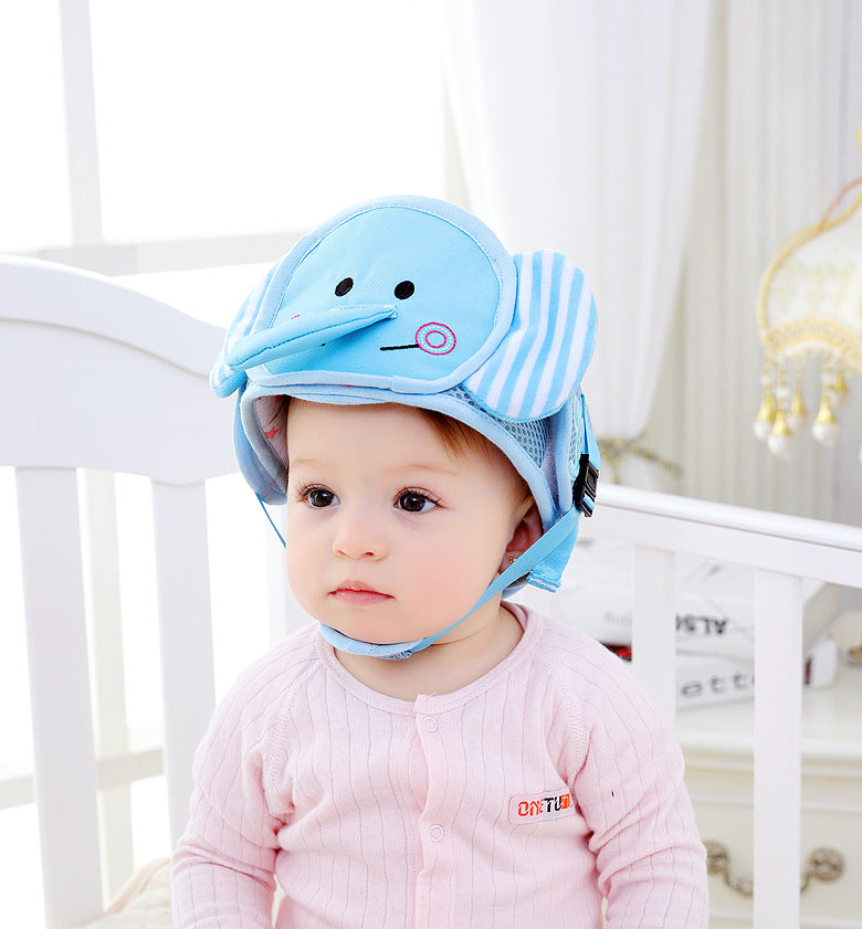 A baby wearing a pink onesie and a blue elephant-themed safety helmet sits in a white crib, surrounded by soft lighting and pastel decor.