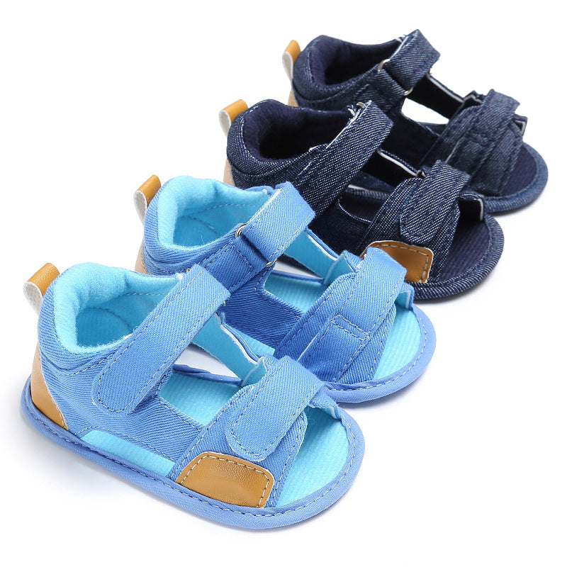 Two pairs of baby sandals, one pair in light blue and the other in dark blue, both with brown accents and velcro straps, displayed on a white background.