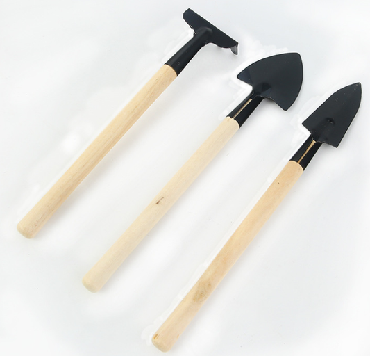Three miniature garden tools with wooden handles and black metal heads, including a rake, hoe, and shovel, are arranged side by side on a white background.