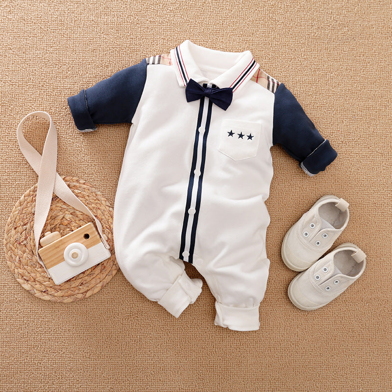 Baby outfit with a white and navy romper featuring a bow tie and three-star pocket design, paired with beige shoes. A wooden toy camera is placed beside it on a woven mat.