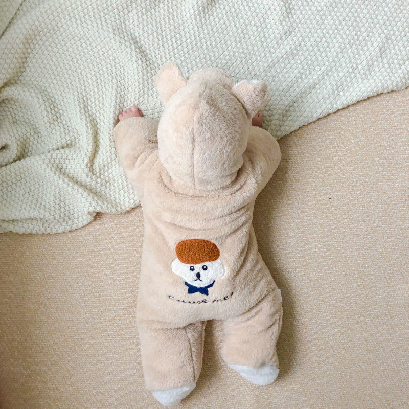 A baby in a cozy bear onesie crawls on a beige carpet, with a white textured blanket nearby. The onesie's back features an embroidered character with a brown hat.