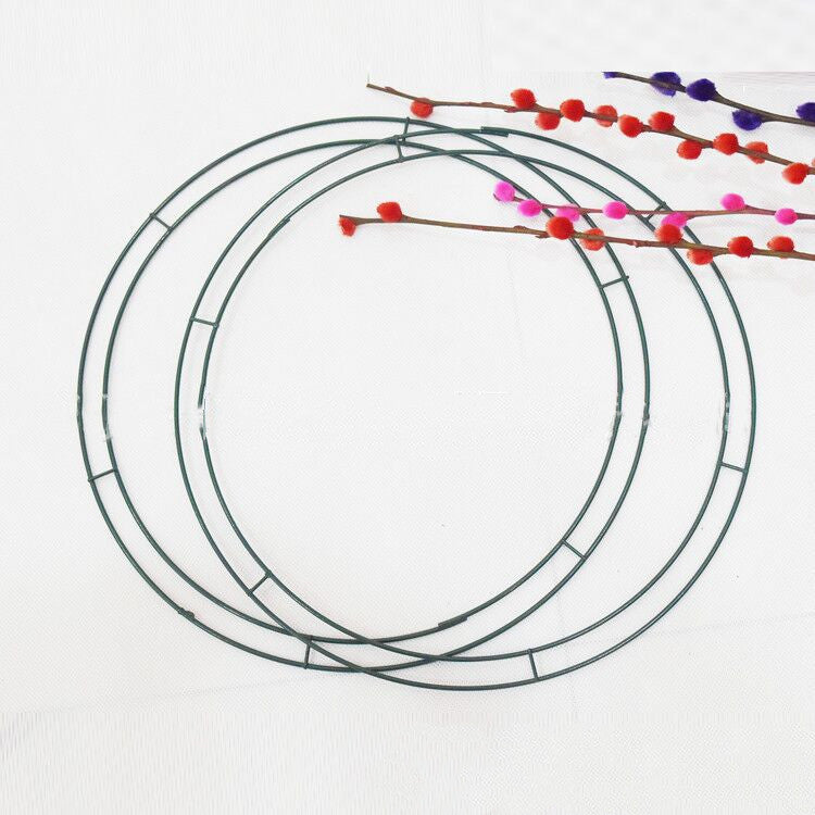 Three green metal rings overlap on a white background. Colorful branches with red, pink, and purple pom-poms extend diagonally across the top right corner.