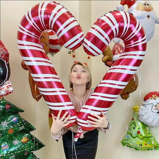 Person holding giant candy cane balloons shaped like a heart, surrounded by holiday-themed balloons, including a Christmas tree and Santa. The person is wearing reindeer antlers.