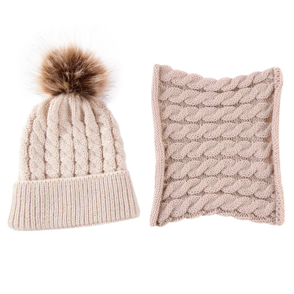 Beige knit beanie with a fur pom-pom and matching cable-knit cowl scarf, displayed side by side on a white background.