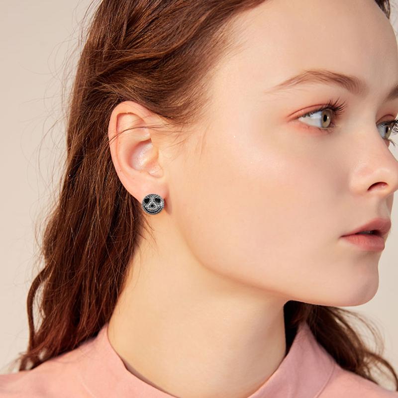 Profile of a woman with long hair wearing a pink top and Jack Skellington stud earrings, looking to the side against a neutral background.
