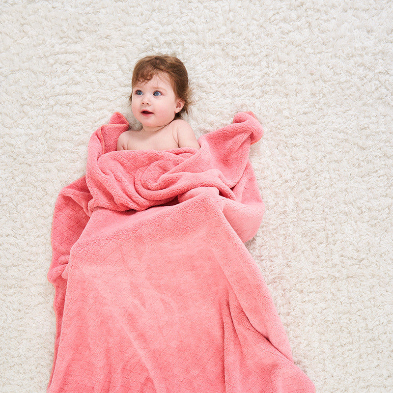 A baby wrapped in a pink blanket lies on a soft, white carpet, gazing upwards with an expression of wonder.