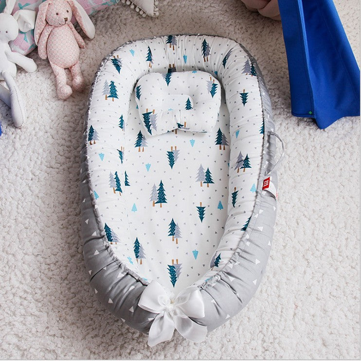 Baby nest with tree patterns and a bow on a soft carpet, surrounded by plush toys and a blue blanket.