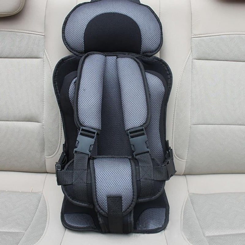 Gray and black child car seat with safety harness sits on a beige car seat. The car seat features padded shoulder and headrest sections, with adjustable straps and buckles.