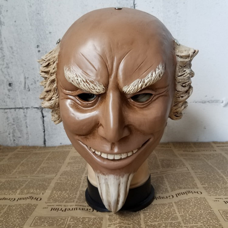 A realistic puppet head features a mischievous grin, bushy eyebrows, and aged white hair, set against a backdrop of old newspaper and a textured wall.