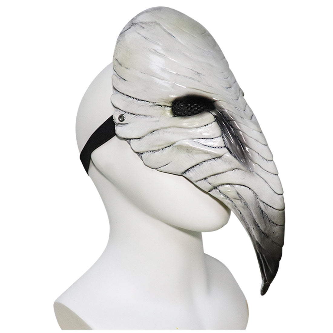 White beak-shaped mask on mannequin head with black strap, featuring detailed grooves and lines resembling feathers, reminiscent of a plague doctor's mask.
