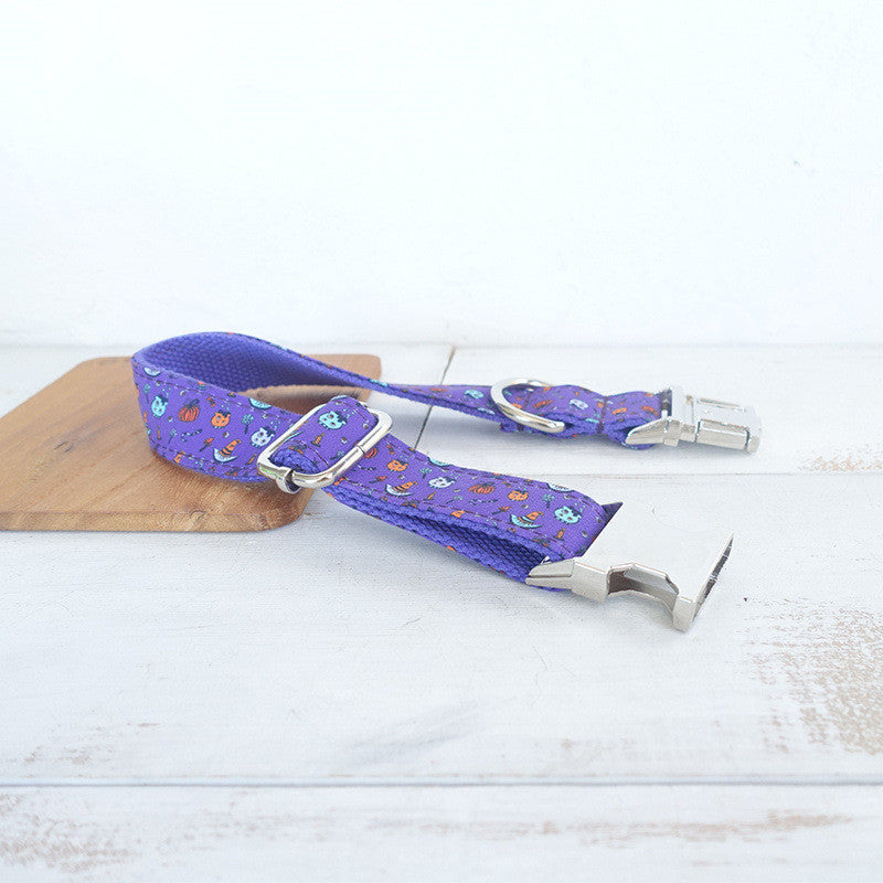 Purple dog seat belt adorned with playful cartoon ghosts and Halloween pumpkins, featuring adjustable strap, metal buckle, and hook, placed on a light wooden surface.