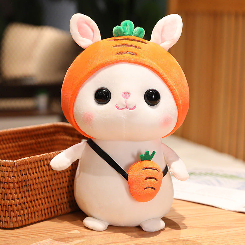 Cute white plush toy with a carrot hood and ears, standing on a wooden surface next to a brown wicker basket, holding a small carrot bag.