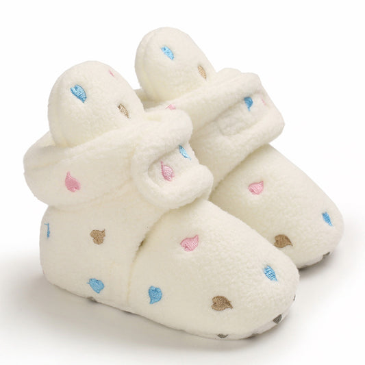 Cozy white baby booties with soft plush texture, adorned with small blue, pink, and brown embroidered raindrop patterns, and Velcro strap closure, set against a plain background.