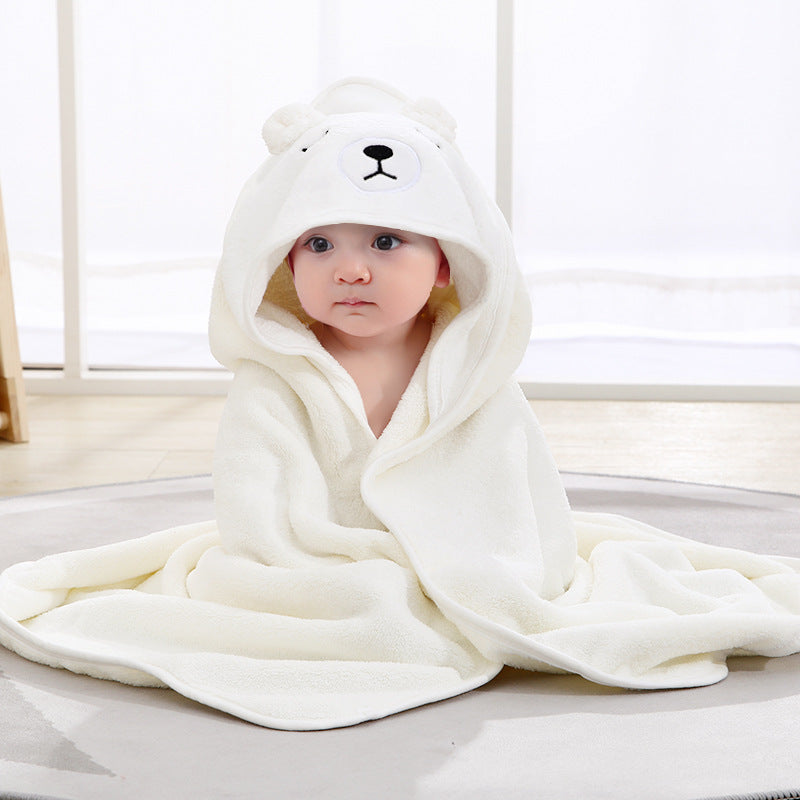 A baby wrapped in a soft, white bear-themed hooded blanket sits on a light-colored rug. The hood up with bear ears and face detailing enhances the cute appearance.