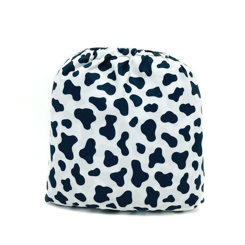 Drawstring bag with a cow print pattern. The fabric is white with irregular black spots, resembling a cowhide. The bag's shape is rounded at the top and flat at the base.