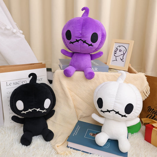 Three plush toys with stitched mouths, big eyes, and sprouting tops in black, purple, and white. They sit on and around books with a beige cloth and minimalistic decor.