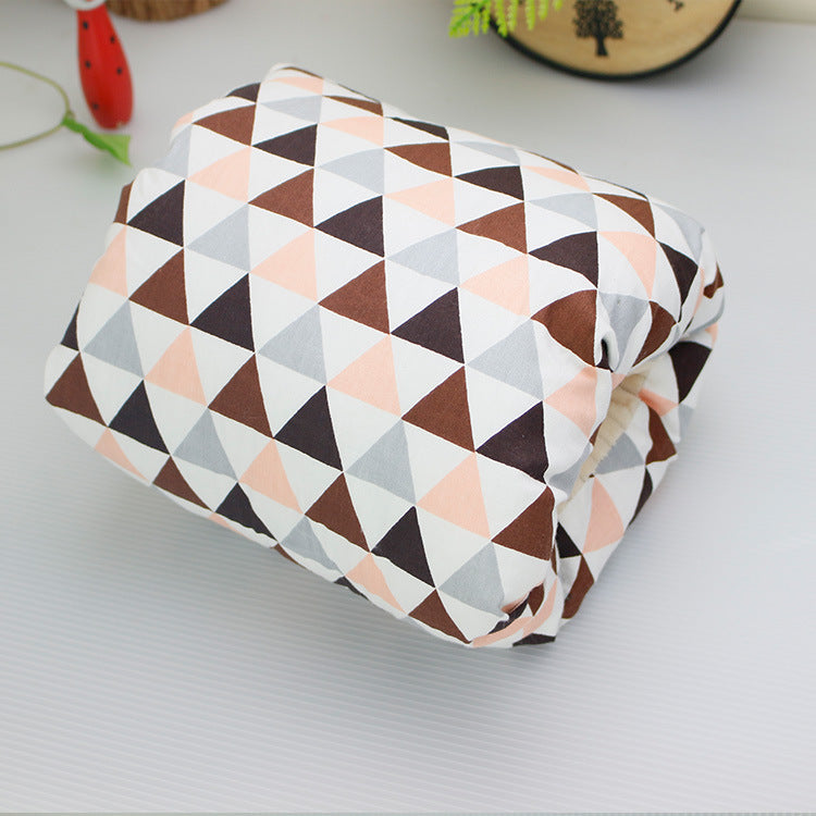Folded blanket with a geometric pattern of pink, brown, and gray triangles on a white background. The blanket is placed on a white surface with decorative items around.