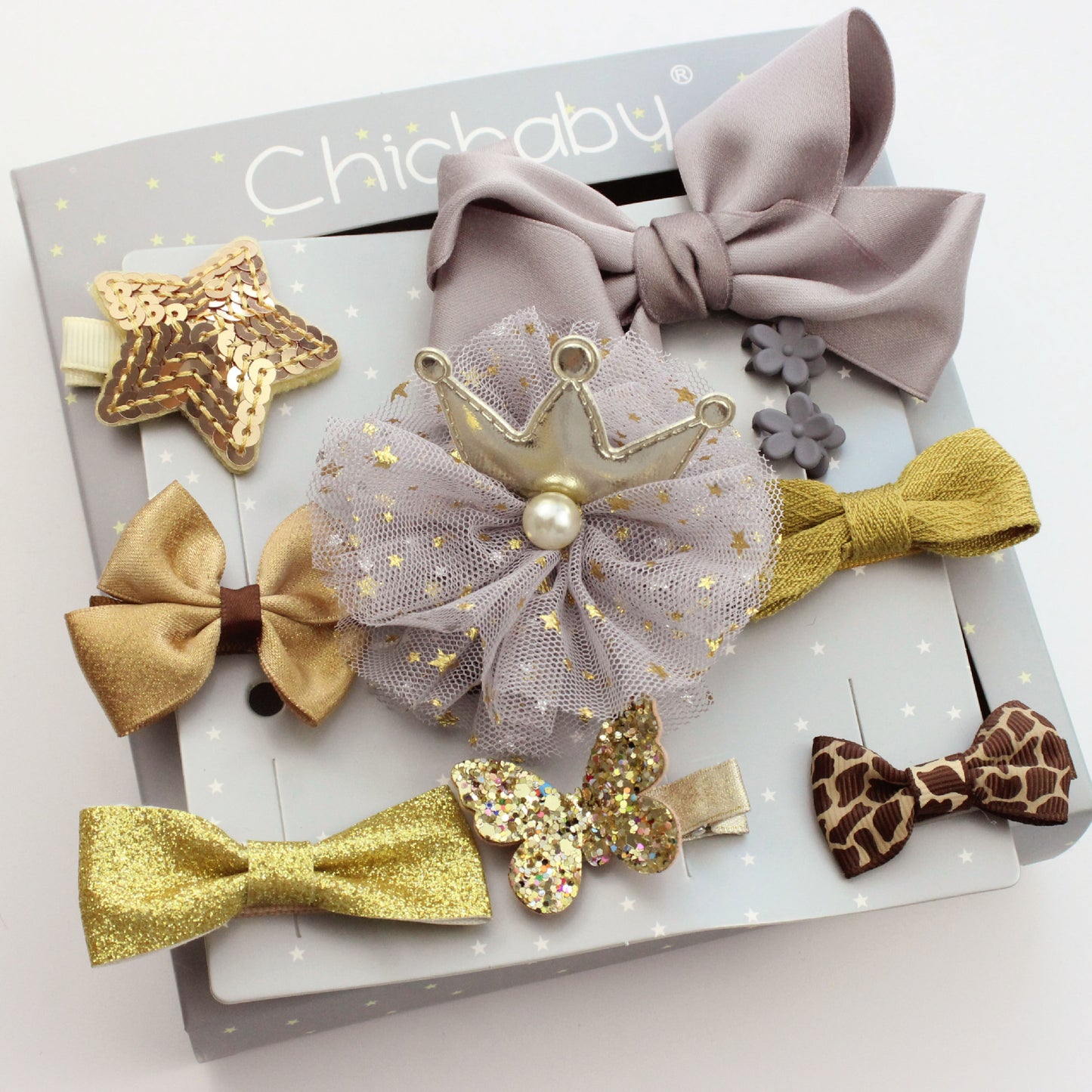 Assorted decorative hair clips on a display card, featuring bows, a sequined star, a glittery butterfly, and a tulle rosette with a crown, in shades of gold, silver, and brown.