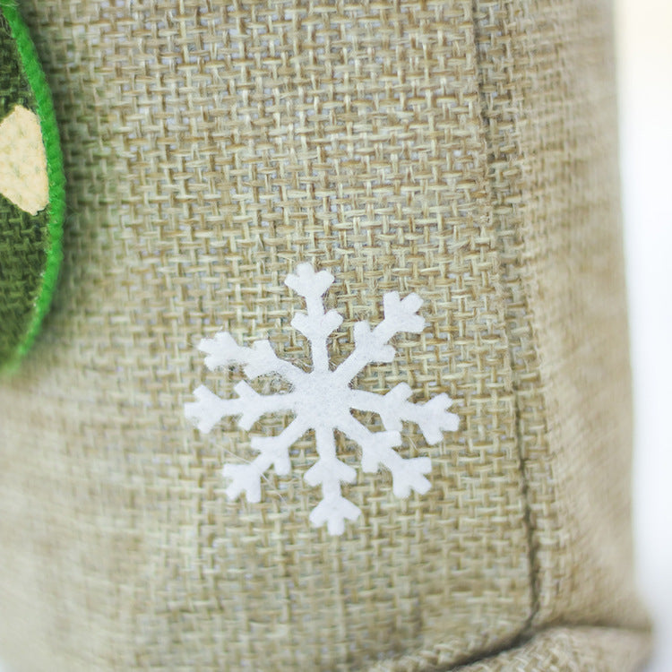 A white felt snowflake embellishment on a textured burlap surface, with a partial view of a green felt ornament on the left.