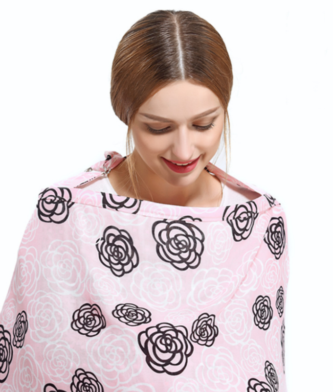 Woman smiling, wearing a pink floral-patterned nursing cover. Her hair is neatly tied back, and she looks downwards. The cover features black and white flower designs.