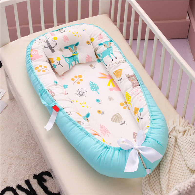 Baby nest in a crib with pastel colors, featuring a turquoise border and playful animal and plant prints on the interior. A white bow ties the end for added charm.