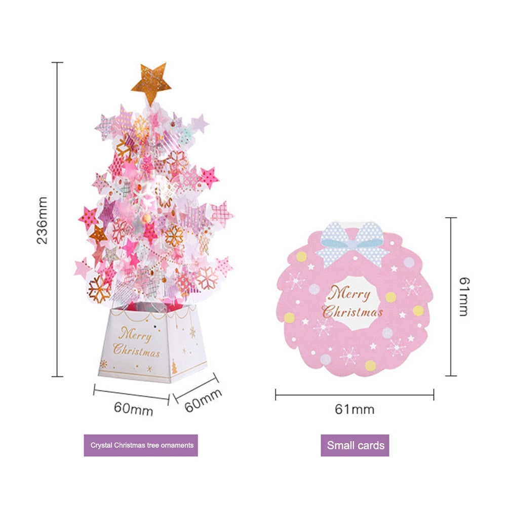 Pink and gold star-shaped ornaments decorate a small 236mm tall Christmas tree with a "Merry Christmas" base. Next to it, a pink 61mm card with a bow matches the festive theme.