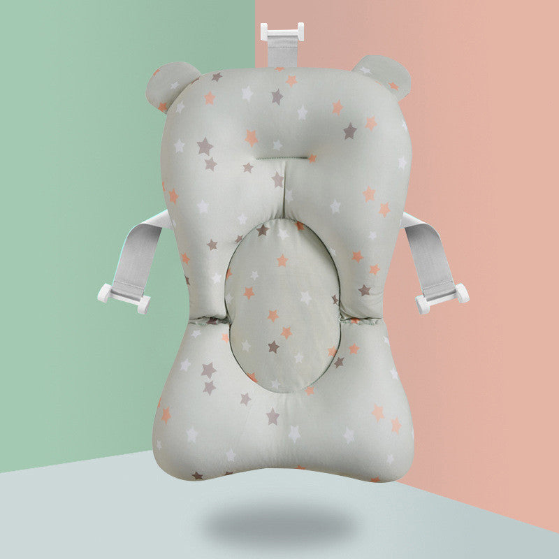 A star-patterned baby bath cushion with side straps, featuring ear-like protrusions at the top, against a dual-colored background of soft green and peach.