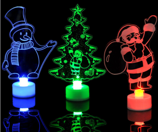 Three glowing LED night lights with Christmas designs: a blue snowman, a green Christmas tree with decorations, and a red Santa holding a sack, all on white bases.