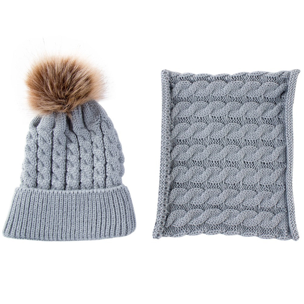 Gray knit beanie with a faux fur pom-pom and matching scarf, both featuring a cable knit pattern.