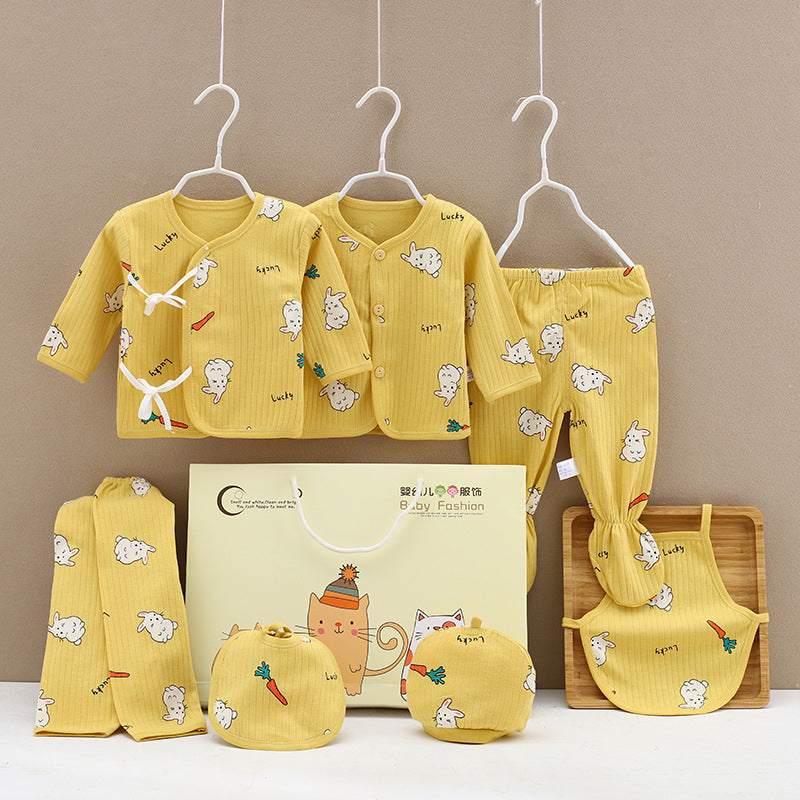 Yellow baby clothing set with bunny and carrot prints, including two tops, pants, bib, mittens, and a gift box. Garments are on hangers against a neutral background.