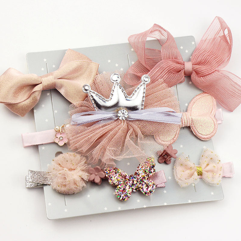 Assorted pink and beige hair clips displayed, featuring bows, a silver crown, a glittery butterfly, and tulle decorations on a starry background.