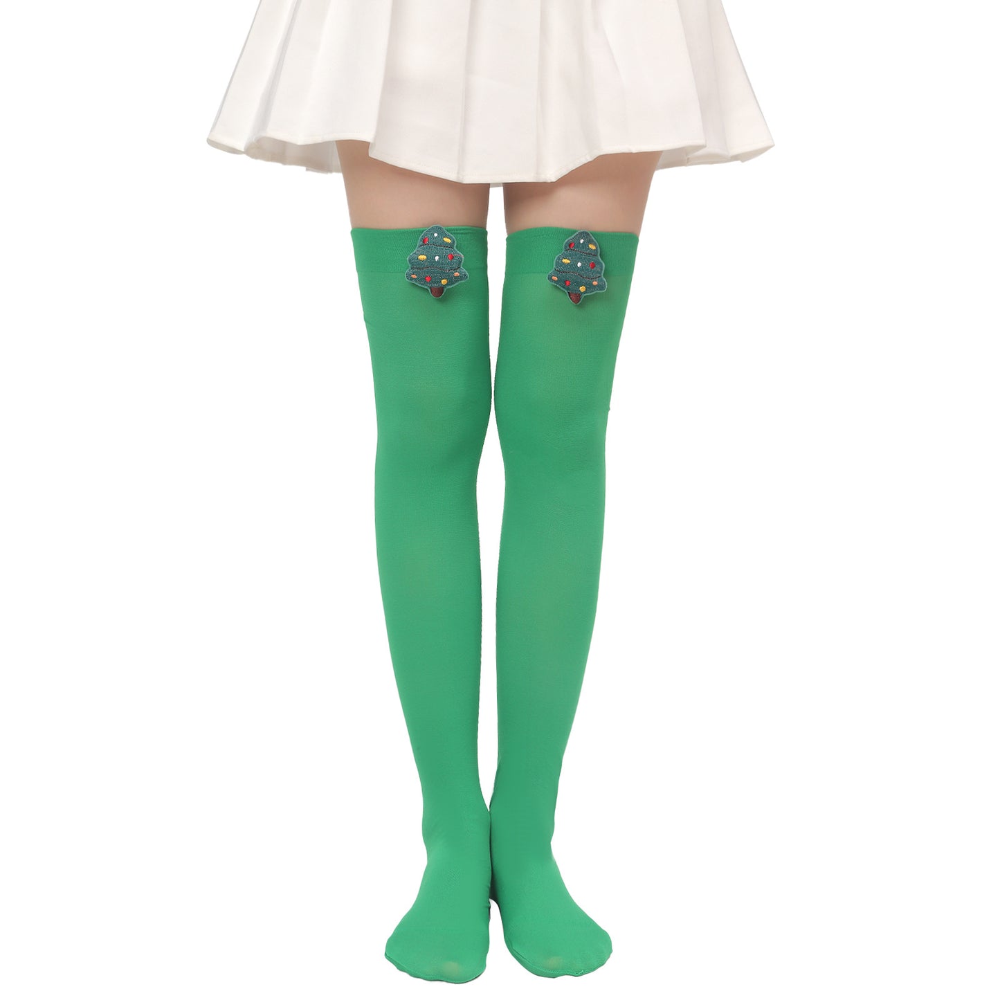 Person wearing green thigh-high socks with Christmas tree patches, standing with feet together, in a white skirt against a white background.
