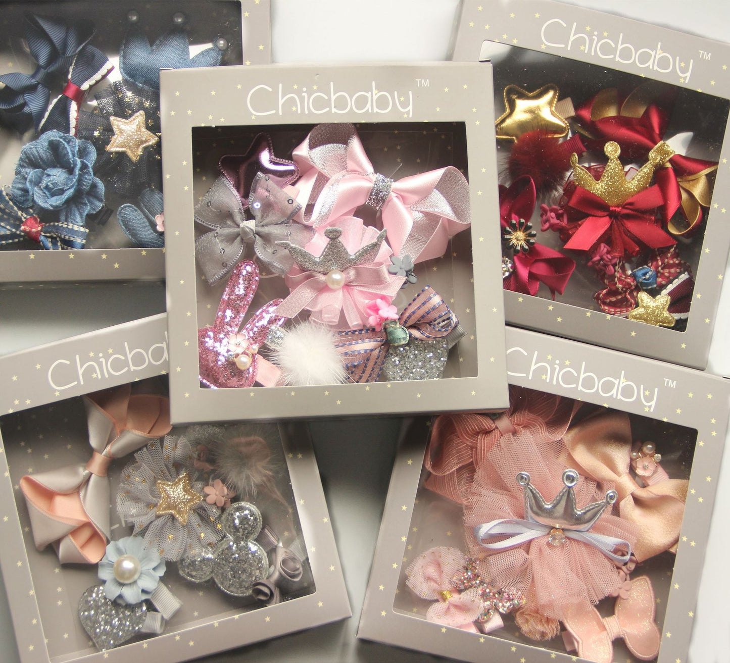 Gift boxes featuring assorted decorative hair clips for babies. Each box displays bows and accessories in various colors and designs, like stars, crowns, and floral prints.