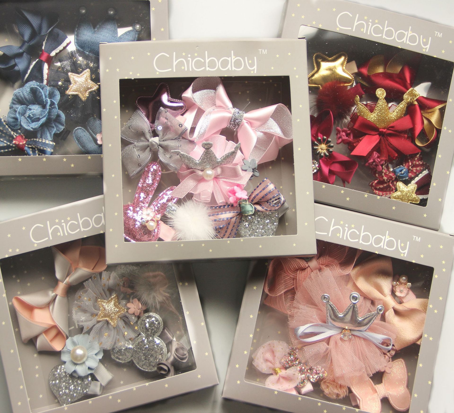 Gift boxes featuring assorted decorative hair clips for babies. Each box displays bows and accessories in various colors and designs, like stars, crowns, and floral prints.