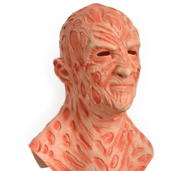 A latex mask with a textured, scarred appearance, featuring deep red and pink tones. The mask has hollow eyes and an unsettling expression, resembling burnt, damaged skin.