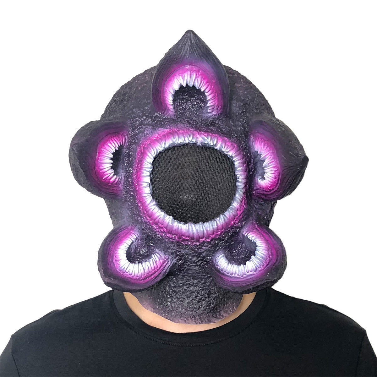 Person wearing a textured, purple mask with multiple eye-like protrusions and a central black mesh over the face, giving an alien or monster appearance.