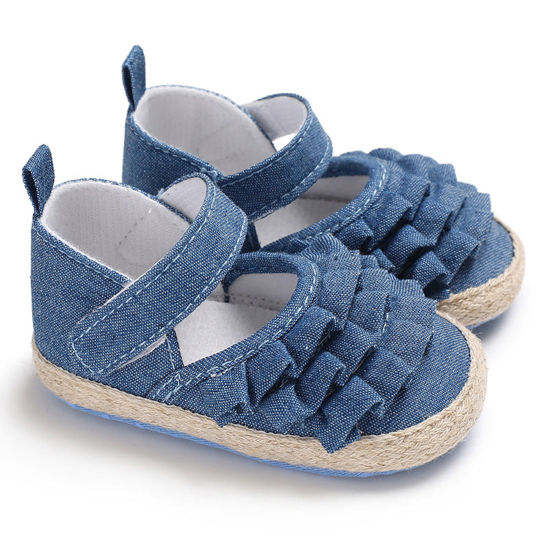 Blue baby shoes with ruffled denim fabric, velcro straps, and woven jute-like soles. They feature a soft, white interior lining and decorative tabs on the back.