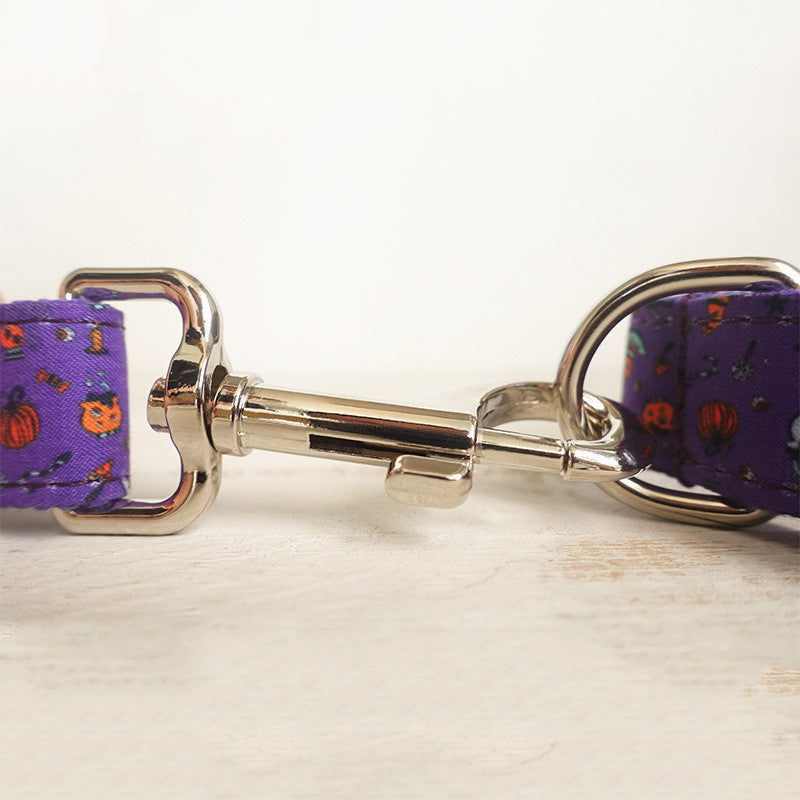 Close-up of a metal clasp connecting two purple pet collars with Halloween-themed patterns, featuring small pumpkins and designs, set on a light surface.