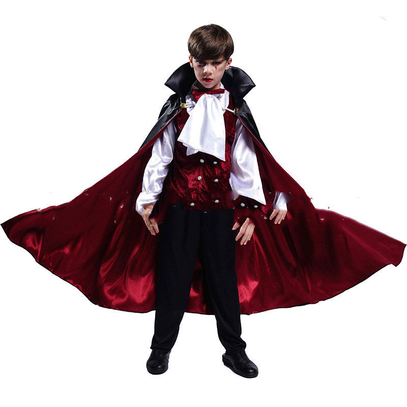 Young boy in a vampire costume with a red and black cape, white shirt, and dark trousers, posing dramatically with arms extended, revealing the cape's interior.
