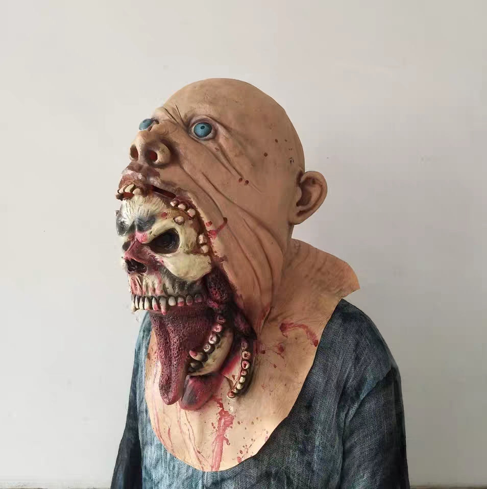Grotesque horror mask with two faces, one above the other; blue eyes, exposed skeletal features, and bloody details. Upper face is bald; lower face appears monstrous.