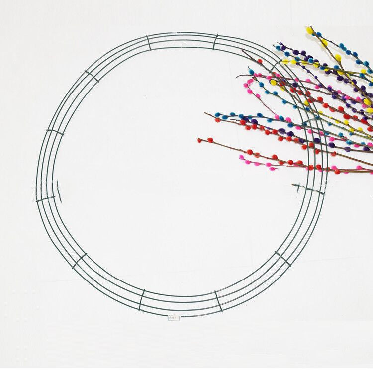 Wire frame circle with colorful pom-pom branches extending from the right side. The flowers are in vibrant shades of blue, pink, red, yellow, and purple against a white background.