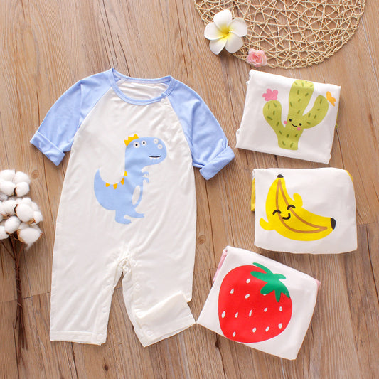 Baby romper with a blue-sleeved dinosaur print, surrounded by folded tops featuring cactus, banana, and strawberry designs, placed on a wooden floor with cotton and flowers.